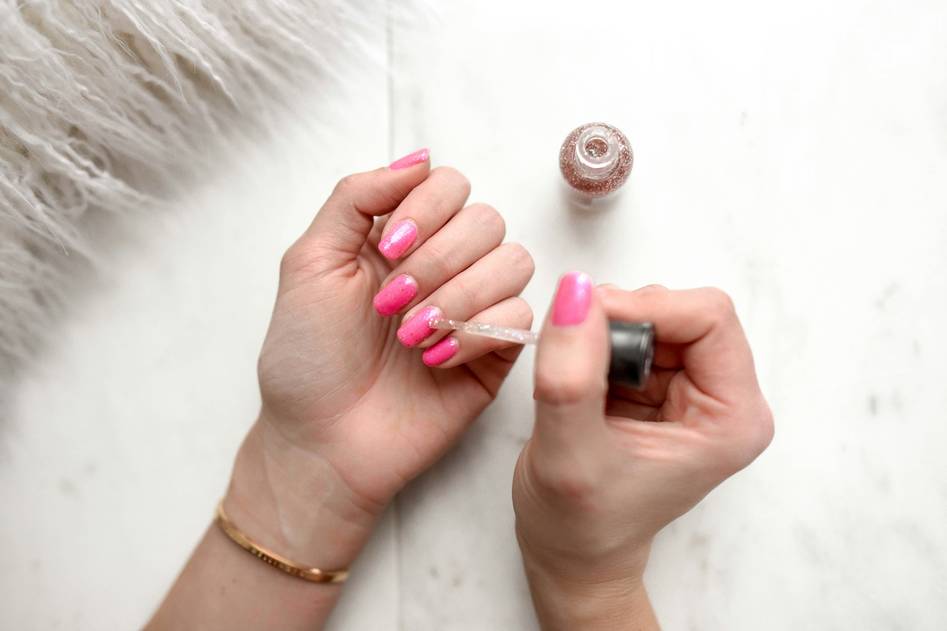 Beauty blogger applying clear top coat to fresh pink nail art